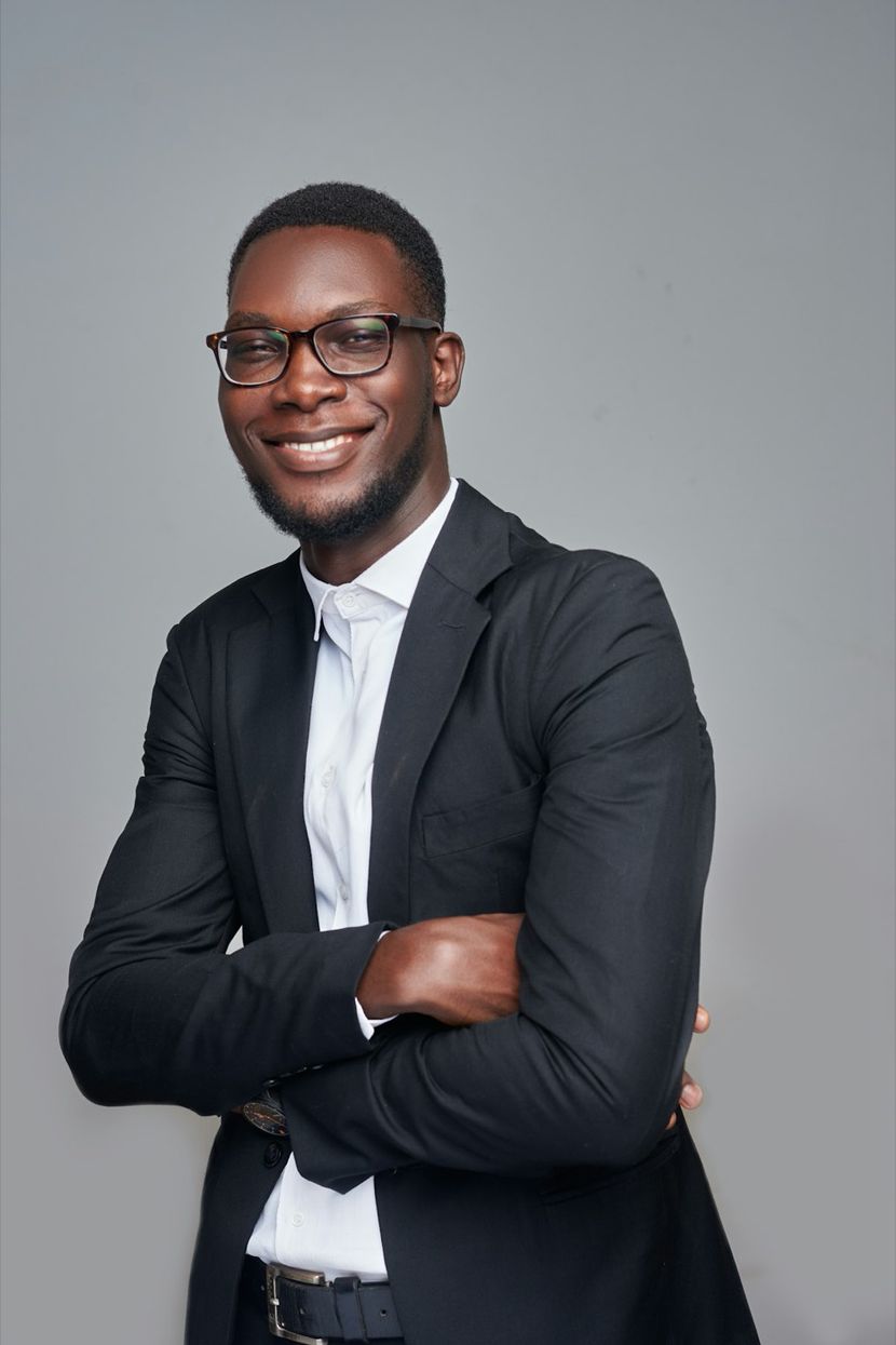 Marcus O. Adebayo, a man in glasses and a dark suit, smiling against a gray backdrop