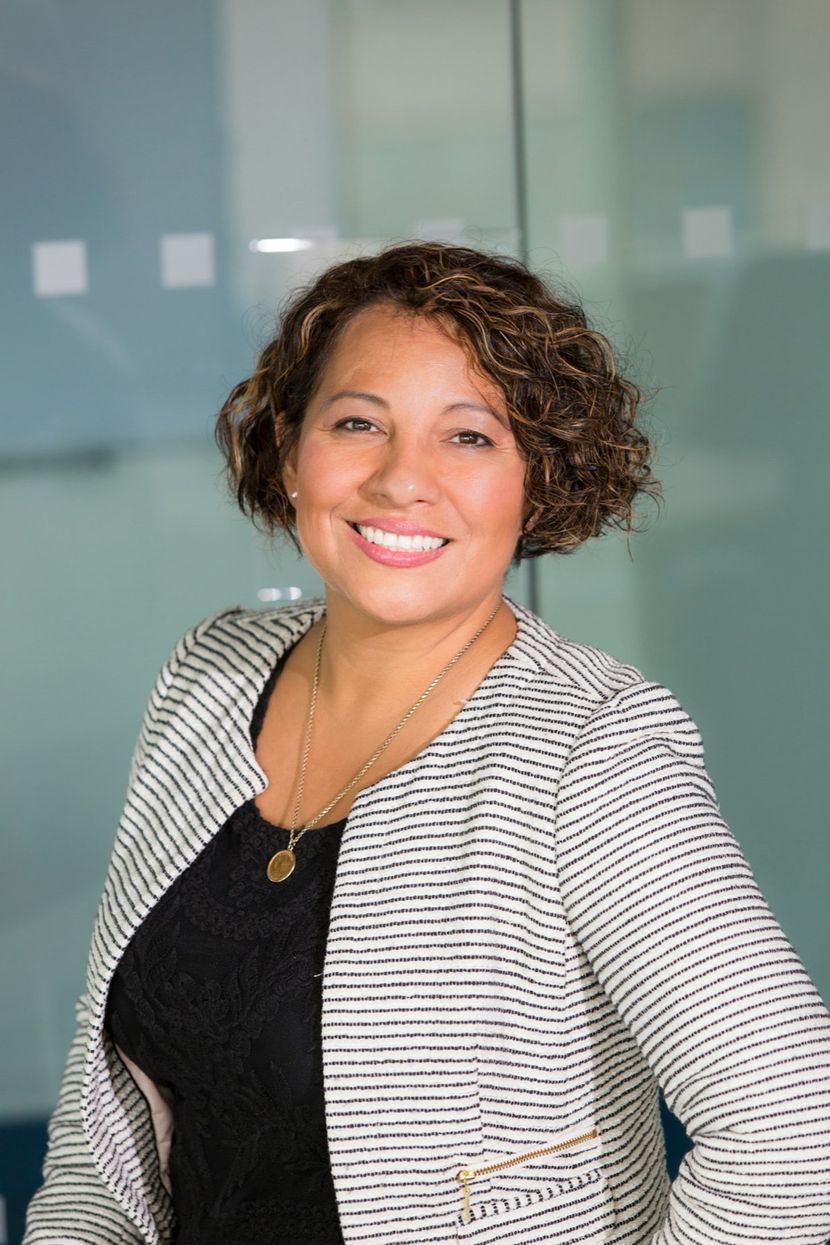 Monica Alvarez, a woman with short curly hair in a striped blazer, smiling in an office