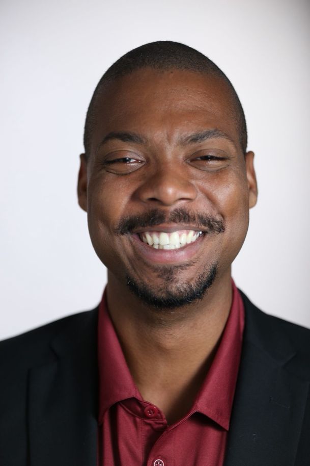 Andre Mitchell, smiling, in a dark suit and maroon shirt