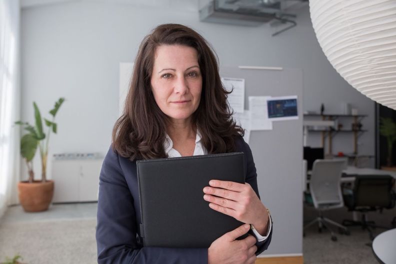 Laura Reyes, a woman with dark hair in a navy blazer, holding a binder in the firm’s office